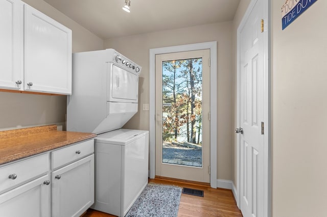 washroom with light hardwood / wood-style floors, cabinets, and stacked washer / dryer