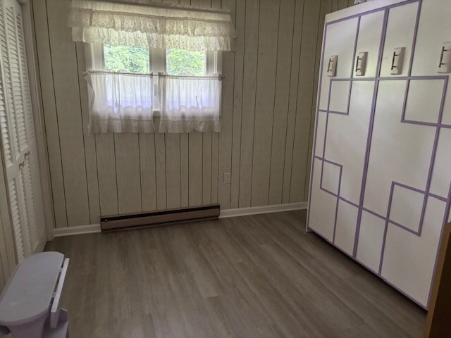 890 Gordon Way, Montross, VA 22520 - unfurnished bedroom featuring a baseboard radiator, baseboards, wood finished floors, and wooden walls