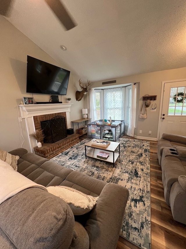 living room with ceiling fan, hardwood / wood-style floors, a textured ceiling, lofted ceiling, and a fireplace