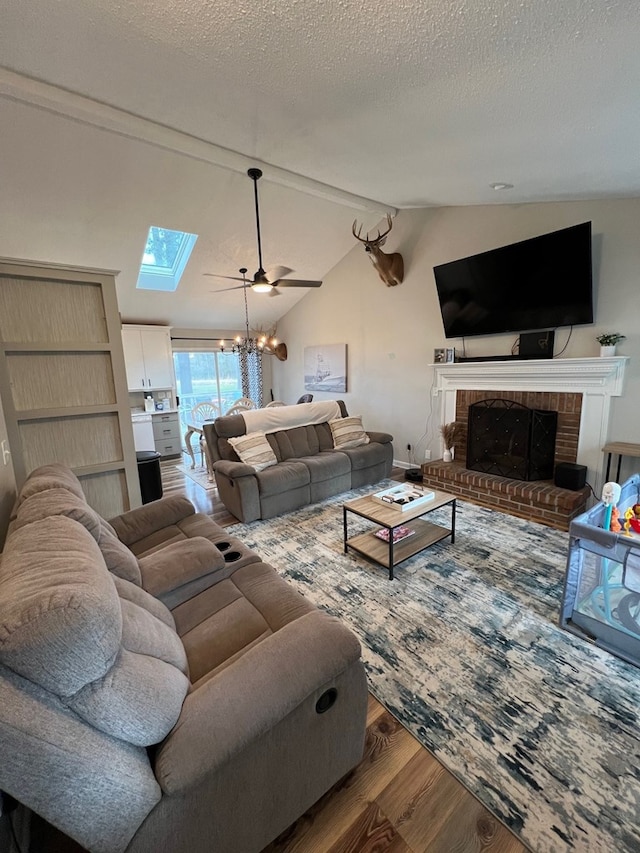 living room with a brick fireplace, lofted ceiling, a textured ceiling, ceiling fan with notable chandelier, and hardwood / wood-style flooring