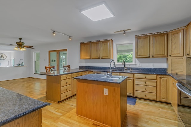 kitchen with ceiling fan, sink, light hardwood / wood-style flooring, kitchen peninsula, and an island with sink