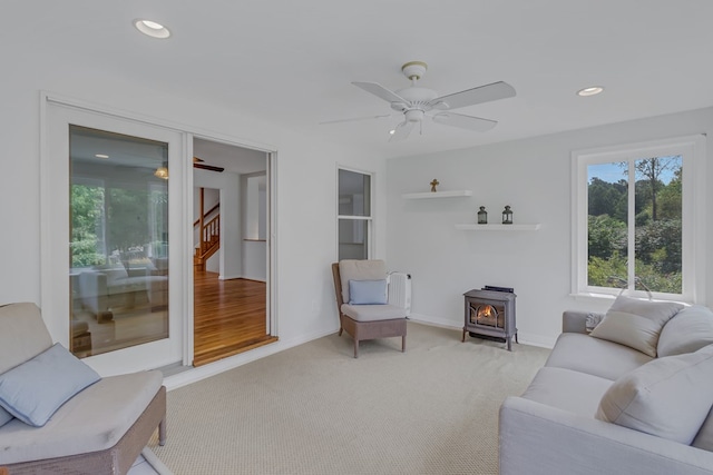 carpeted living room featuring a wood stove and ceiling fan