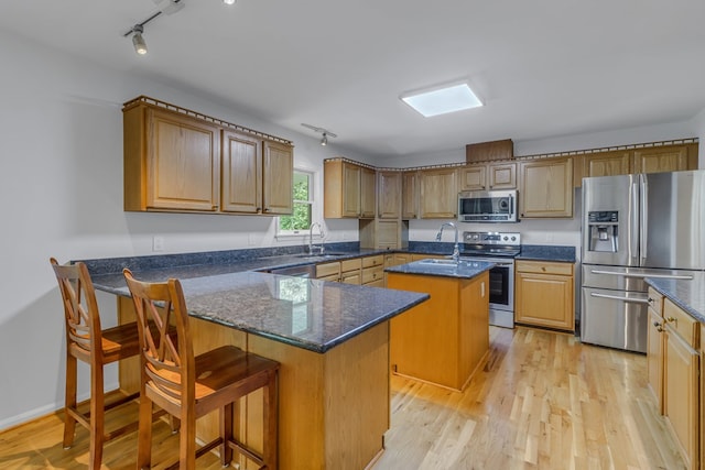 kitchen featuring appliances with stainless steel finishes, a kitchen island with sink, sink, light hardwood / wood-style flooring, and a breakfast bar area