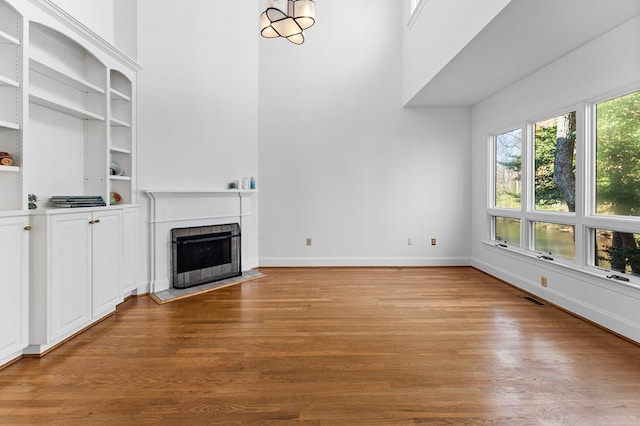 unfurnished living room featuring light wood-type flooring, built in features, and a tile fireplace