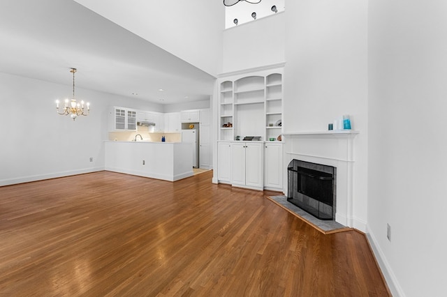 unfurnished living room with dark hardwood / wood-style flooring, built in features, a chandelier, and sink