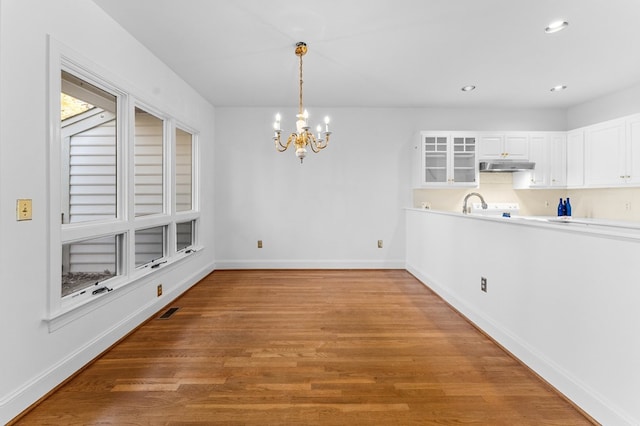 unfurnished dining area featuring sink, light hardwood / wood-style flooring, and an inviting chandelier