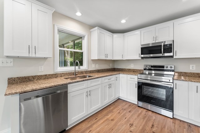 kitchen with appliances with stainless steel finishes, light wood-type flooring, sink, stone countertops, and white cabinetry