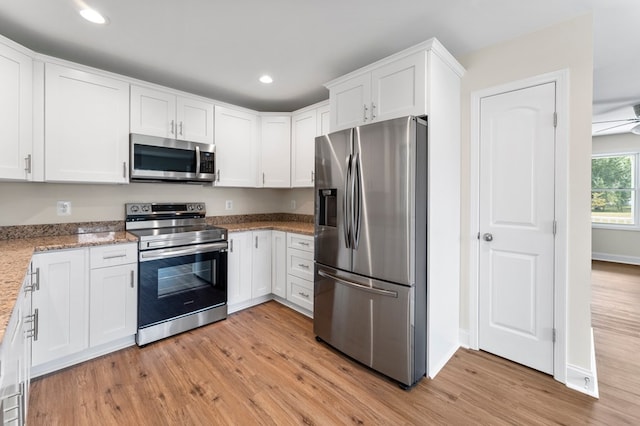 kitchen with light wood-type flooring, stainless steel appliances, white cabinetry, and light stone counters