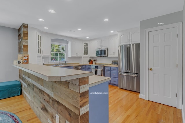 kitchen featuring kitchen peninsula, stainless steel appliances, light hardwood / wood-style flooring, white cabinetry, and a breakfast bar area