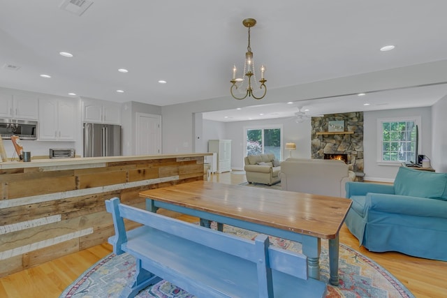 dining area featuring a stone fireplace, a wealth of natural light, a notable chandelier, and light wood-type flooring