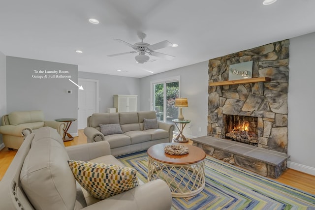 living room with hardwood / wood-style flooring, a stone fireplace, and ceiling fan