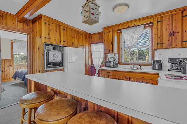 kitchen with a breakfast bar, sink, white fridge, oven, and carpet