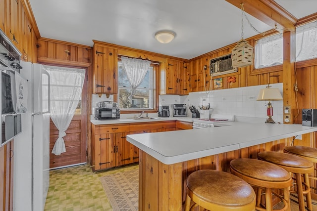 kitchen with sink, white appliances, a kitchen breakfast bar, decorative light fixtures, and kitchen peninsula