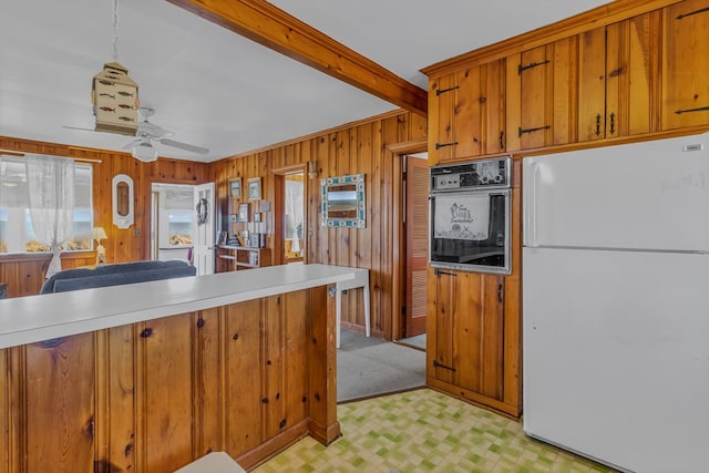 kitchen featuring wood walls, hanging light fixtures, white refrigerator, beamed ceiling, and oven