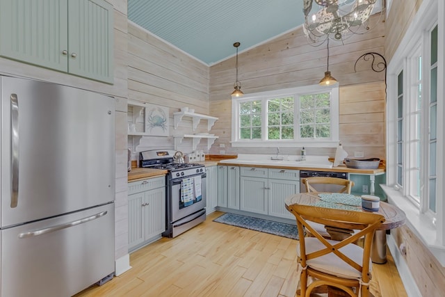 kitchen featuring wood counters, wood walls, decorative light fixtures, appliances with stainless steel finishes, and light wood-type flooring