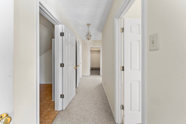 hallway featuring a textured ceiling, light carpet, and baseboards