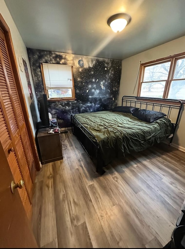 bedroom featuring baseboards, wood finished floors, an accent wall, and wallpapered walls