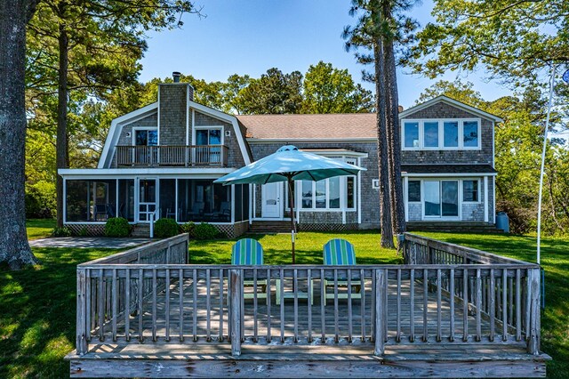 rear view of property featuring a sunroom, a deck, and a lawn