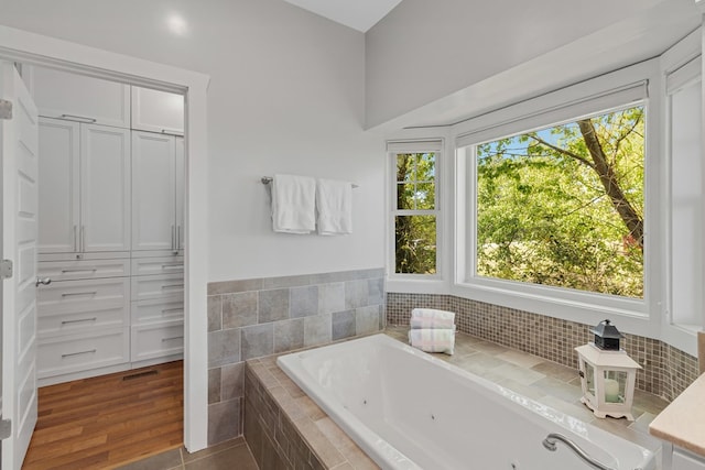 bathroom with a healthy amount of sunlight, tiled bath, and hardwood / wood-style floors