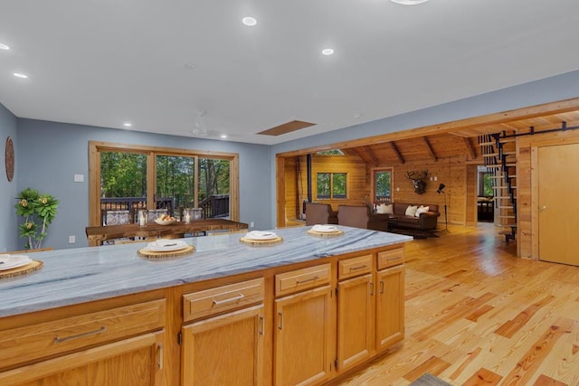 kitchen featuring light wood-type flooring, light stone counters, a wealth of natural light, and wood walls