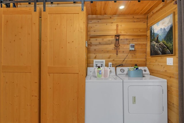 laundry room featuring a barn door, wooden walls, washer and clothes dryer, and wooden ceiling