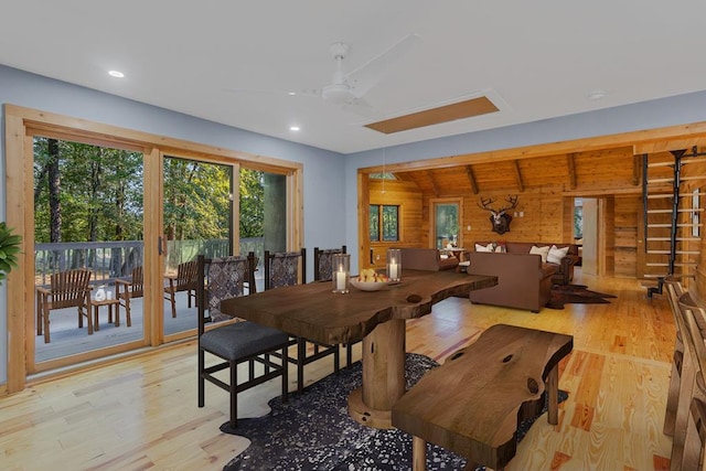 dining space with light hardwood / wood-style floors, vaulted ceiling, ceiling fan, and wood walls