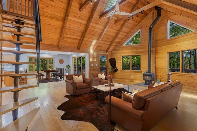 living room with a wood stove, wooden walls, light hardwood / wood-style flooring, beamed ceiling, and wood ceiling