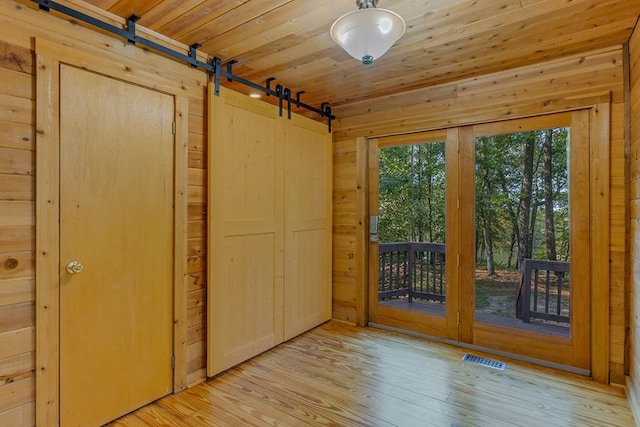 doorway to outside featuring wood walls, a barn door, light wood-type flooring, and wood ceiling