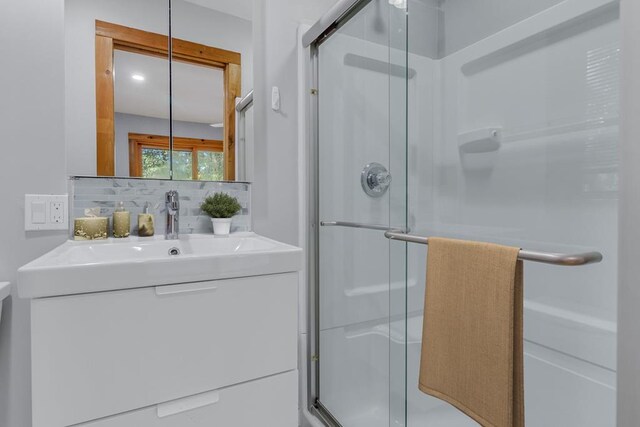 bathroom with vanity, a shower with shower door, and tasteful backsplash