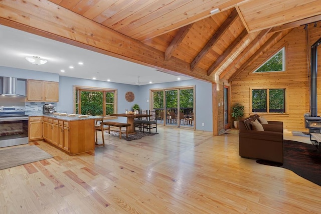 interior space featuring kitchen peninsula, wood ceiling, wall chimney range hood, range, and a wood stove