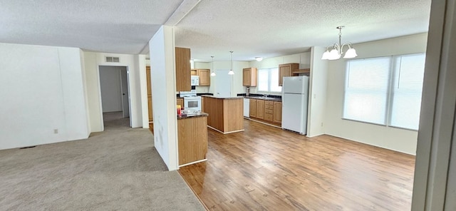 kitchen featuring a center island, white appliances, an inviting chandelier, decorative light fixtures, and light colored carpet