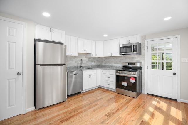 kitchen with sink, light wood-type flooring, white cabinets, stainless steel appliances, and backsplash