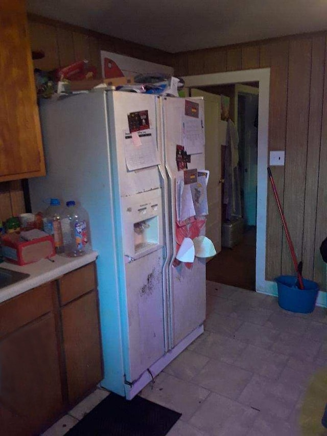 kitchen with white fridge with ice dispenser, brown cabinets, light countertops, and light floors