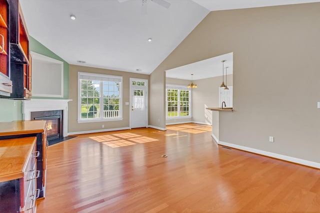 unfurnished living room featuring baseboards, ceiling fan with notable chandelier, wood finished floors, and a premium fireplace