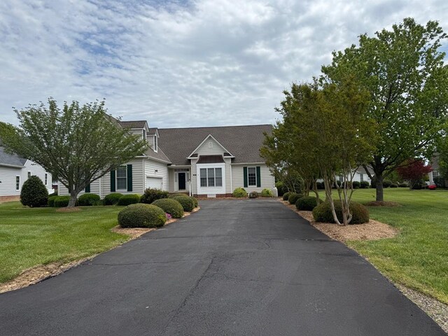 cape cod house with an attached garage, driveway, a shingled roof, and a front lawn