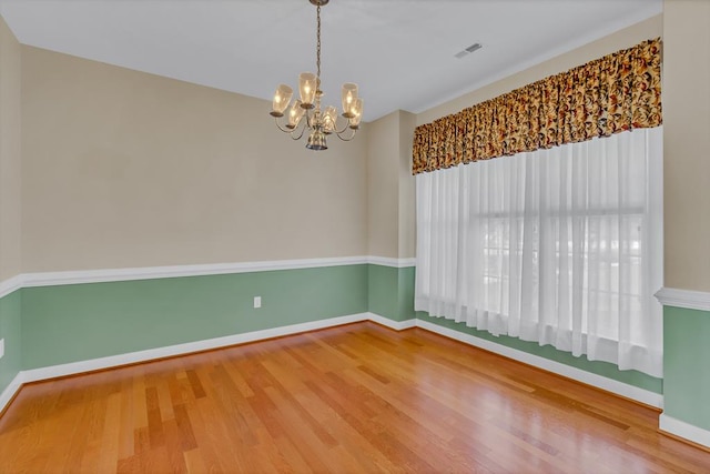 unfurnished room with baseboards, a chandelier, wood finished floors, and visible vents