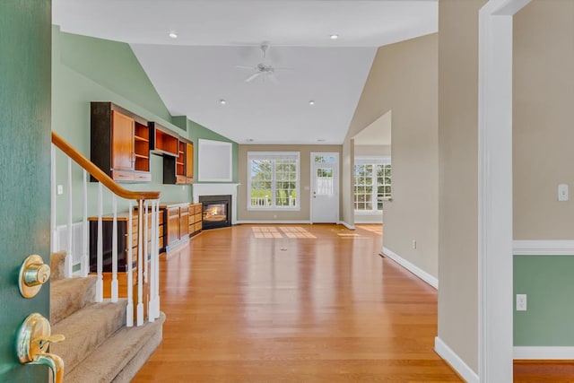 unfurnished living room featuring a ceiling fan, light wood finished floors, a glass covered fireplace, and stairway