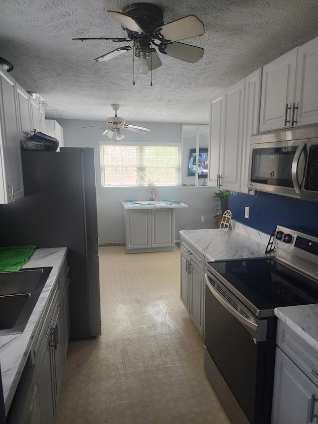 kitchen with a sink, appliances with stainless steel finishes, light stone countertops, light floors, and ceiling fan