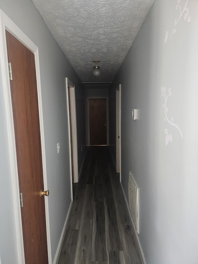 hall with dark wood finished floors, visible vents, a textured ceiling, and baseboards