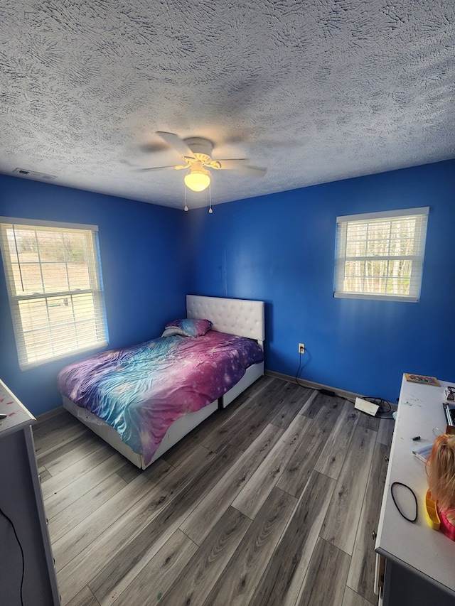 bedroom featuring a ceiling fan, wood finished floors, baseboards, and a textured ceiling