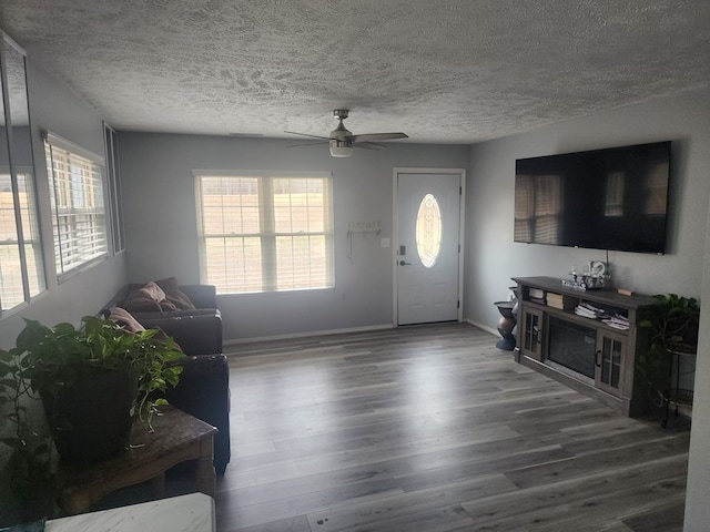 living area with baseboards, a textured ceiling, ceiling fan, and wood finished floors