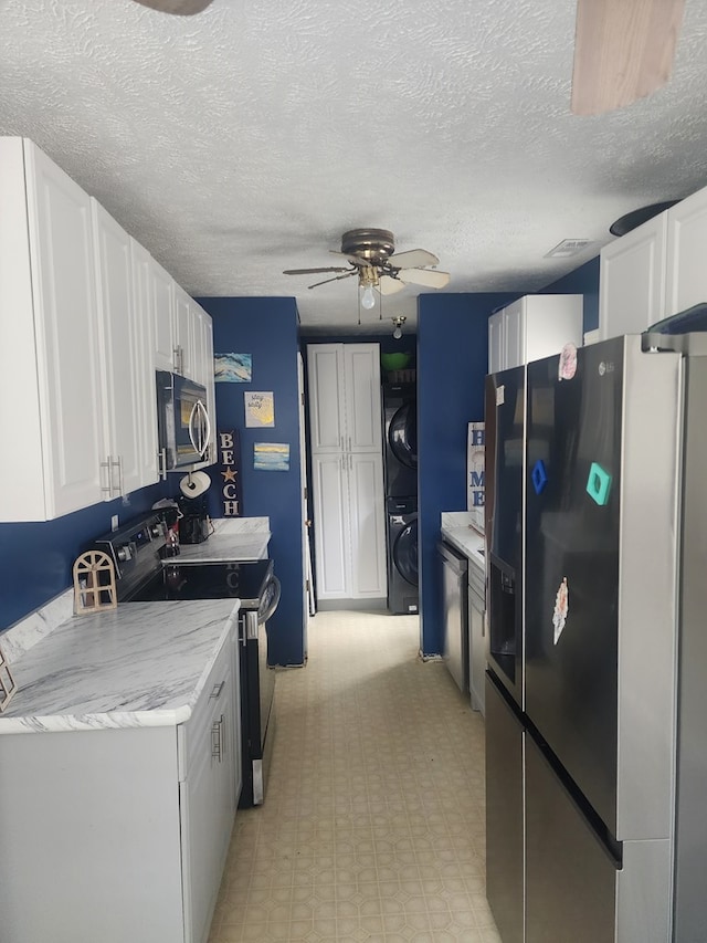 kitchen featuring stainless steel appliances, white cabinets, a ceiling fan, and stacked washer / dryer