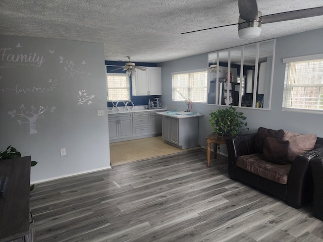 living area featuring baseboards, a textured ceiling, ceiling fan, and wood finished floors