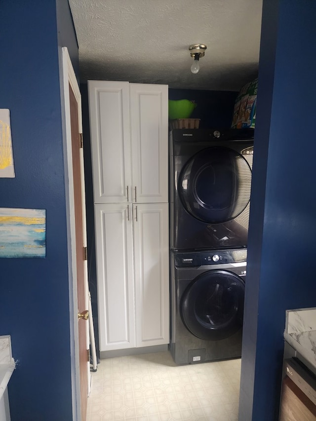 laundry area with tile patterned floors, cabinet space, stacked washer and clothes dryer, and a textured ceiling