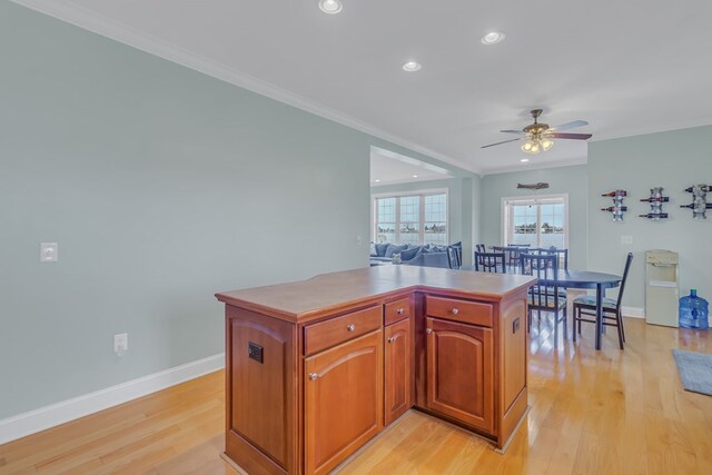 kitchen with ceiling fan, a kitchen island, crown molding, and light hardwood / wood-style flooring