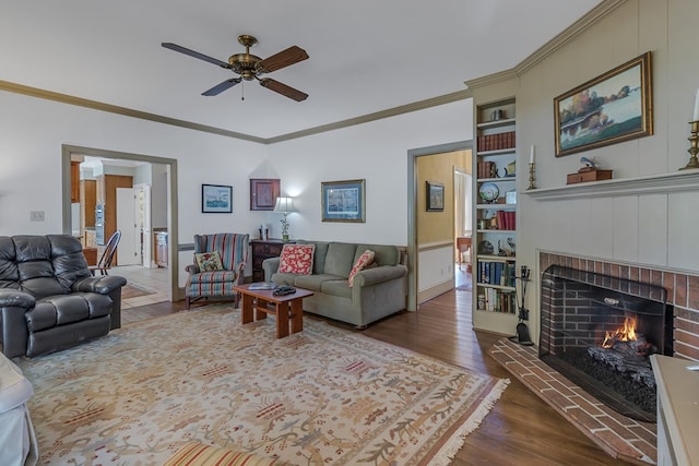 living room featuring a brick fireplace, ceiling fan, built in features, ornamental molding, and dark hardwood / wood-style flooring