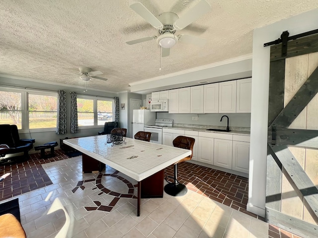 kitchen featuring ornamental molding, white appliances, sink, a barn door, and white cabinets