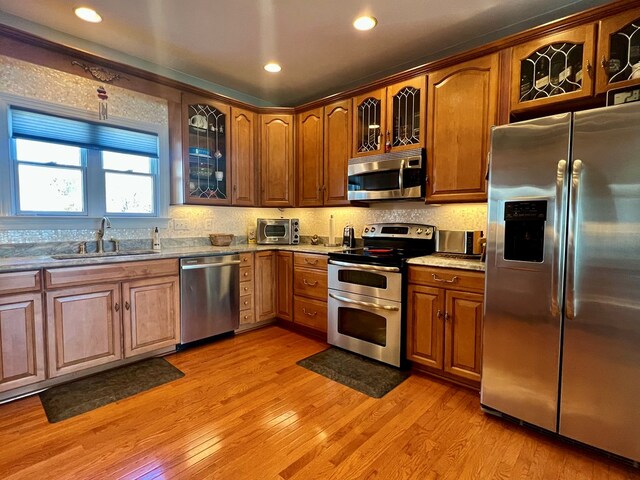 kitchen featuring light wood-type flooring, stainless steel appliances, light stone counters, and sink