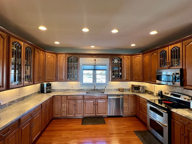 kitchen with appliances with stainless steel finishes, light stone counters, light hardwood / wood-style flooring, and sink