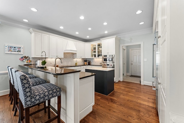 kitchen featuring a breakfast bar, a center island, premium range hood, white cabinets, and kitchen peninsula